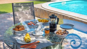 A glass table set outdoors with breakfast items, a coffee maker, and a view of a swimming pool. - El Reposo Alhaurín de la Torre by Ruralidays (Málaga)