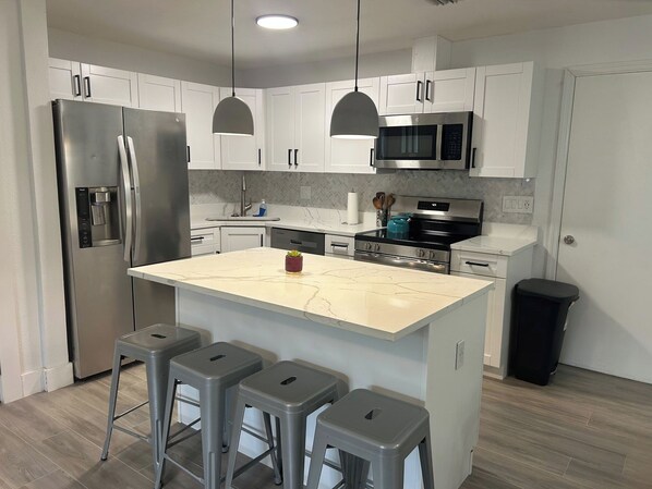 A modern kitchen with white cabinets, stainless steel appliances, a marble island, and bar stools.