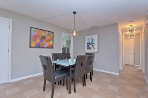 A dining area with a table and chairs, a hanging light fixture, and two framed artworks on the wall.