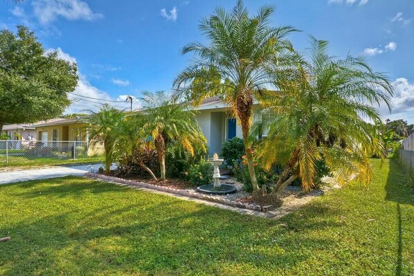 A residential property with a well-maintained lawn, palm trees, and a fountain.