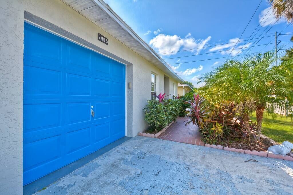 A building with a blue garage door, a number '260' sign, and a small garden with various plants.