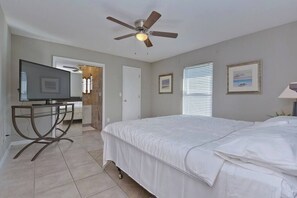 A bedroom with a bed, ceiling fan, television, and a desk with a chair.
