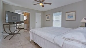 A bedroom with a bed, a ceiling fan, a TV on a stand, and a door leading to a bathroom.