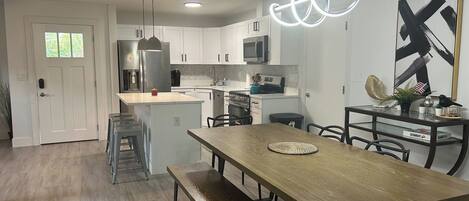 A modern kitchen with white cabinets, a central island, and a dining area with a wooden table and benches.