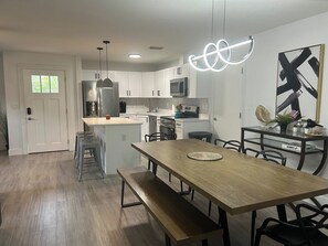 A modern kitchen with white cabinets, a central island, and a dining area with a wooden table and benches.