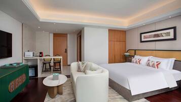 A hotel room with a bed, a sofa, a small table, a TV, and a microwave.