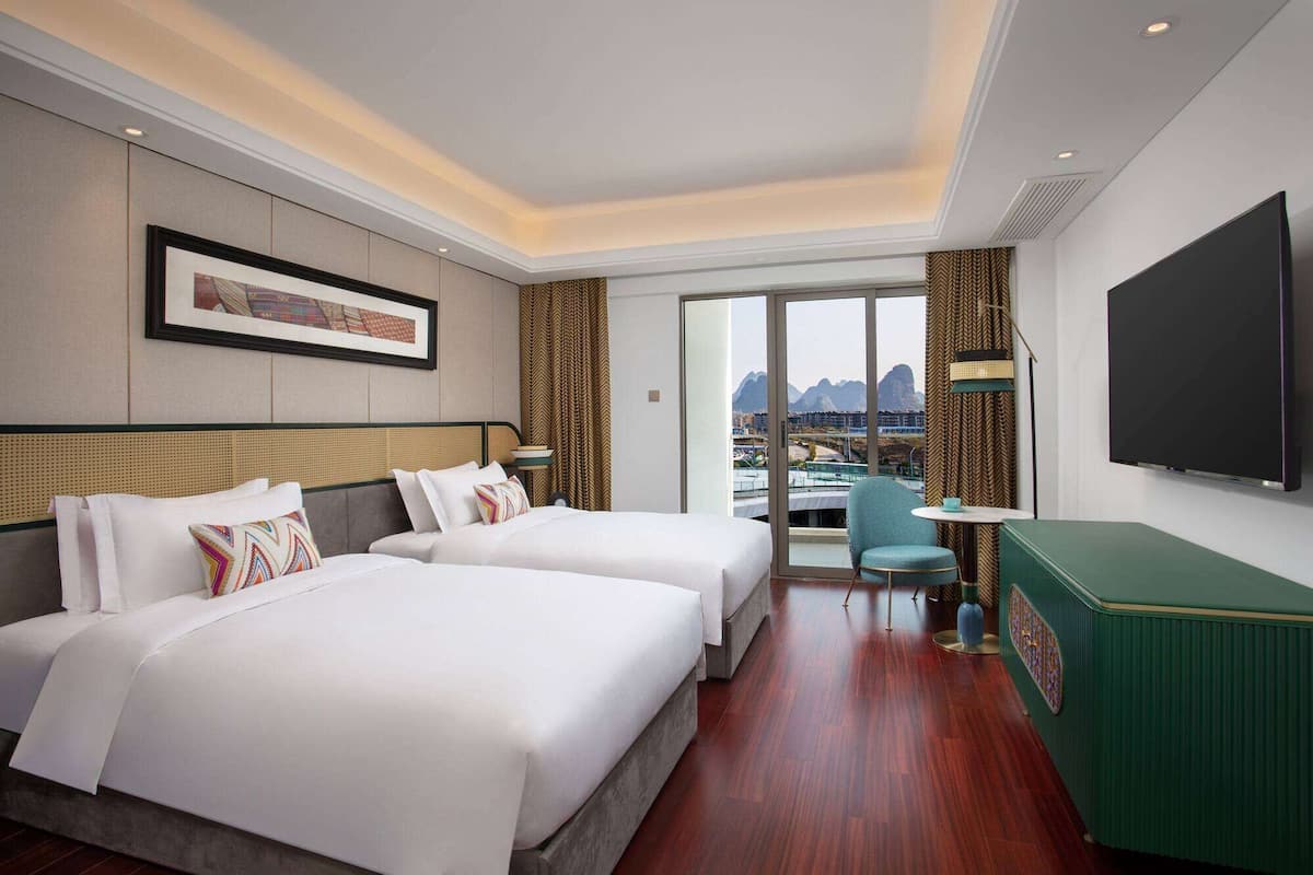 Habitación de hotel con dos camas, televisión, escritorio y vista a la ciudad.
