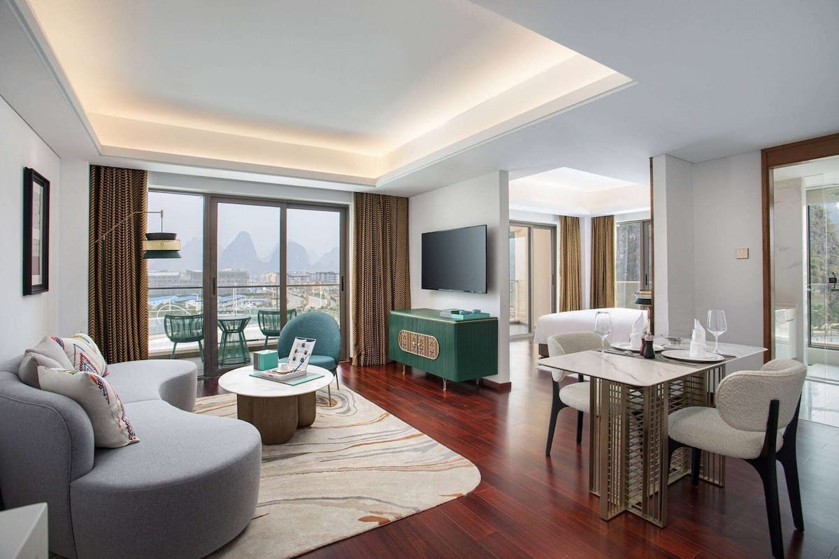Una habitación de hotel moderna con sala de estar, comedor y balcón con vistas a la ciudad.