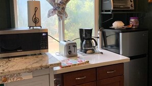 Cocina compacta con microondas, tostadora, cafetera y un refrigerador pequeño.
