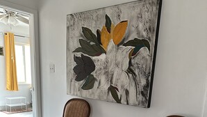 Una habitación con dos sillas de mimbre, una pequeña mesa redonda y un cuadro abstracto grande en la pared.