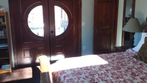 Une chambre à coucher avec un lit, une armoire en bois dotée d’une fenêtre ronde, une table de chevet avec une lampe et une bibliothèque.