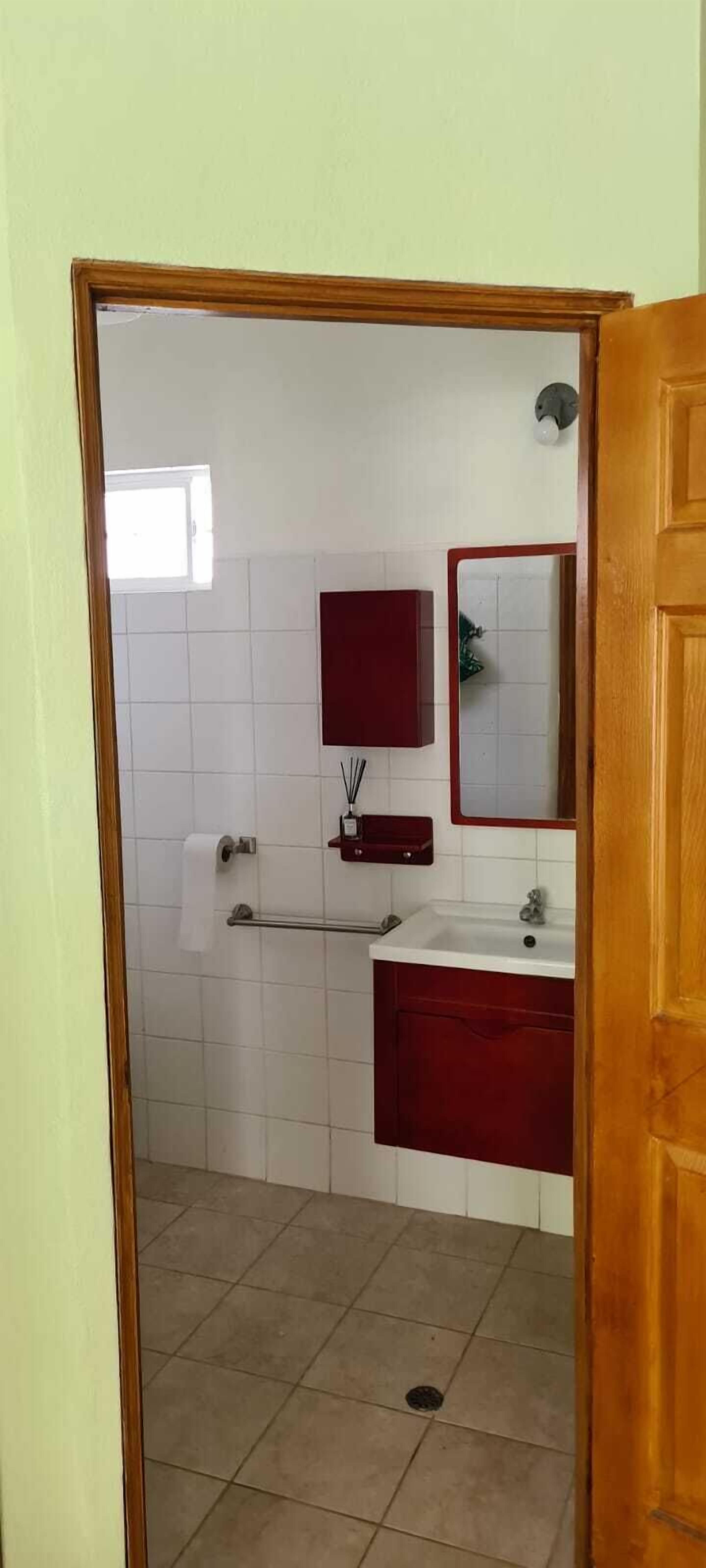 A bathroom with white tiled walls, a red vanity, a mirror, and a toilet.