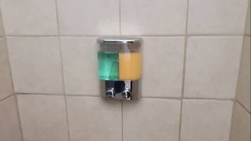 Un box de ducha con azulejos, un dispensador de jabón y un desagüe.