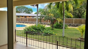 Un balcón con vista a una piscina, una valla de madera y un área verde con palmeras.