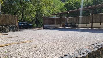 Un aparcamiento de grava con un muro de piedra, una valla de madera y una estructura cubierta.