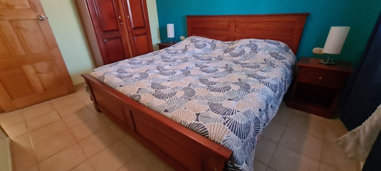 Een slaapkamer met een houten bed, een nachtkastje met een lamp en een deur.