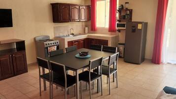 A compact kitchen with a dining area, a stove, a refrigerator, and a flat-screen TV.