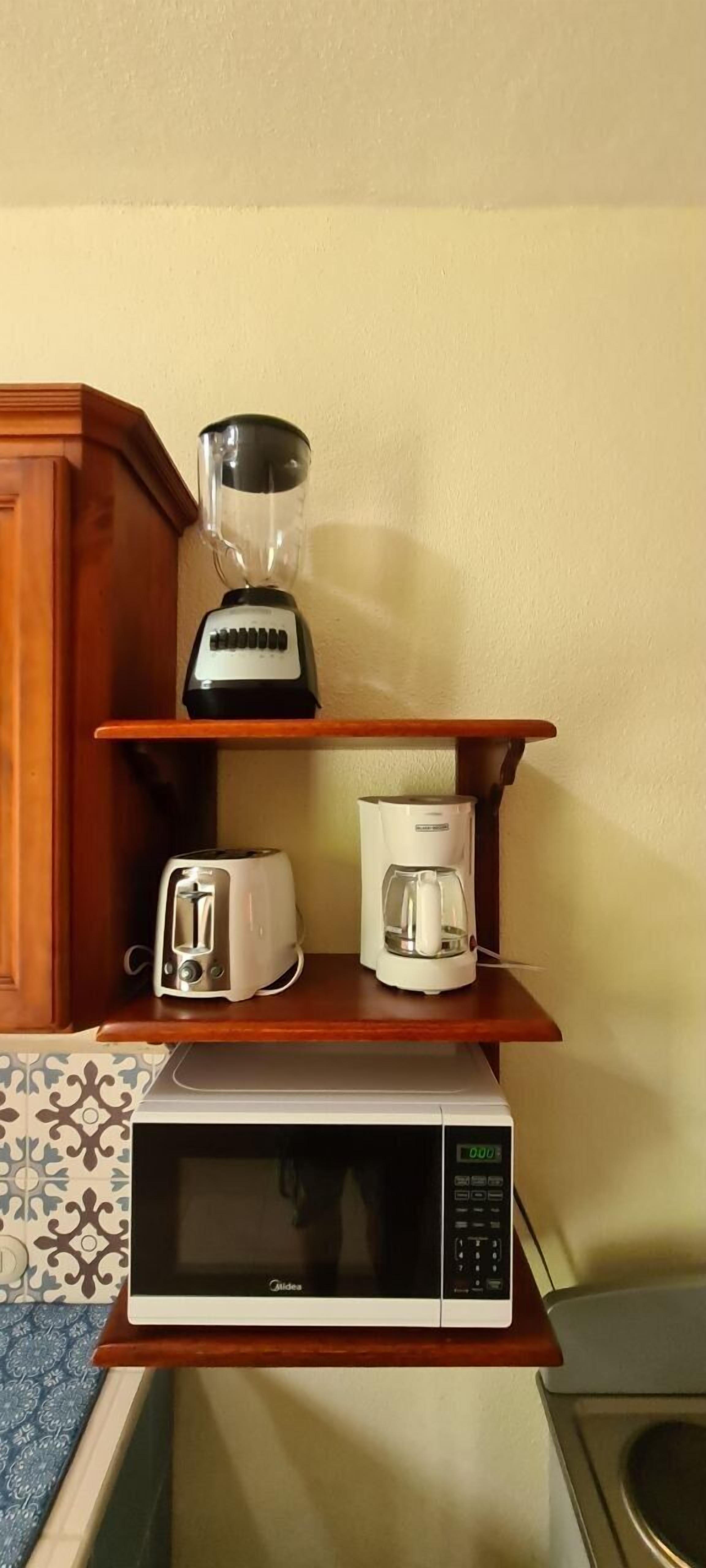 Cucina con forno a microonde, tostapane e macchina del caffè su un ripiano in legno.