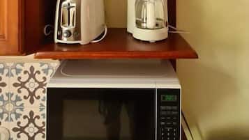 Une cuisine équipée d’un four à micro-ondes, d’un grille-pain et d’une machine à café, le tout posé sur une étagère en bois.