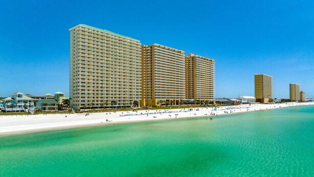 Ein Strandhotel mit mehreren Hochhäusern, einem Sandstrand und klarem türkisblauem Wasser.