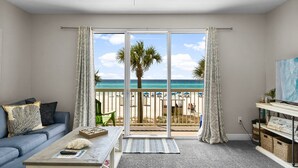 Ein Wohnzimmer mit Blick auf den Strand, einem Deckenventilator und einer Couch mit Kissen.
