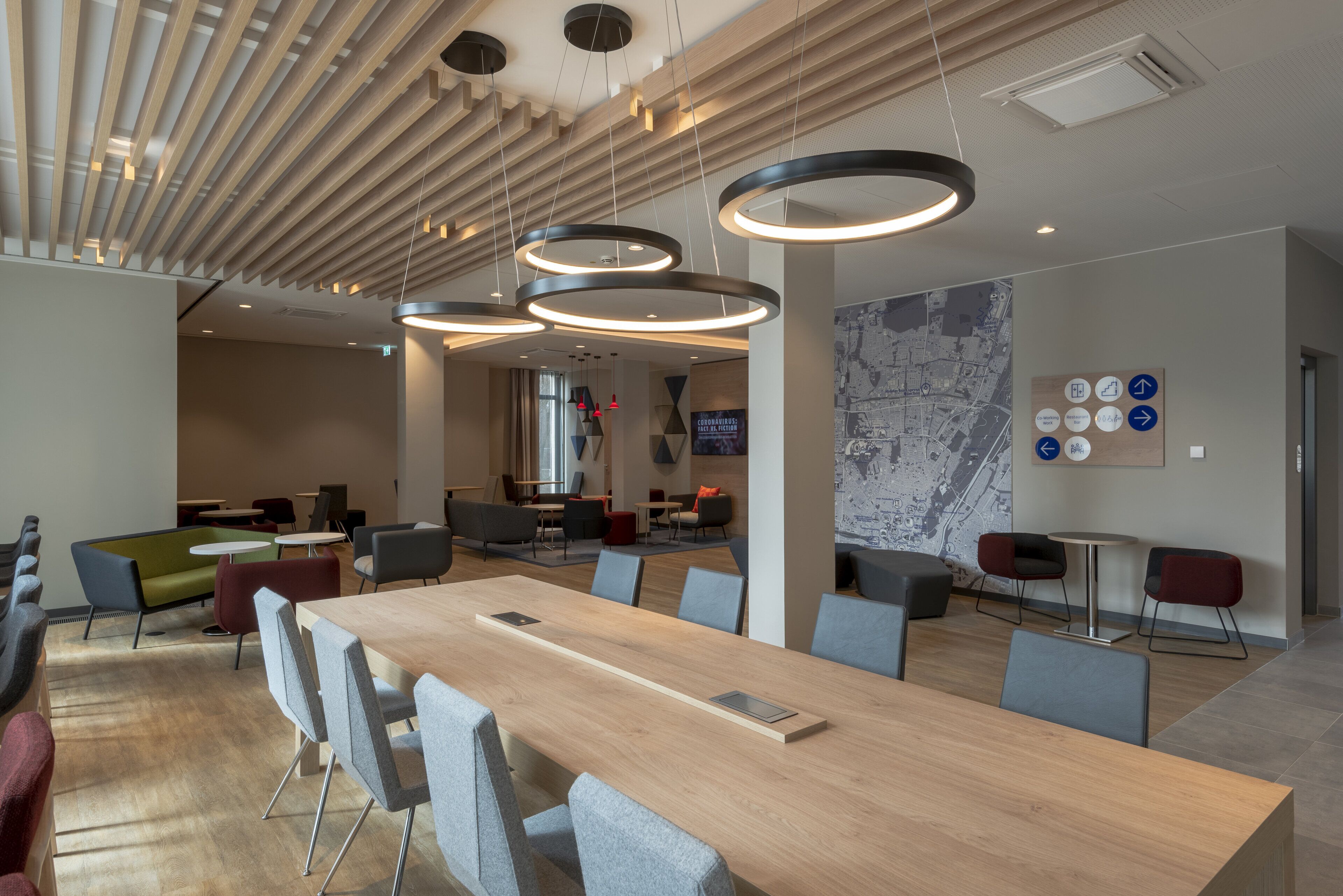 A modern conference room with a long wooden table, grey chairs, and circular pendant lights.