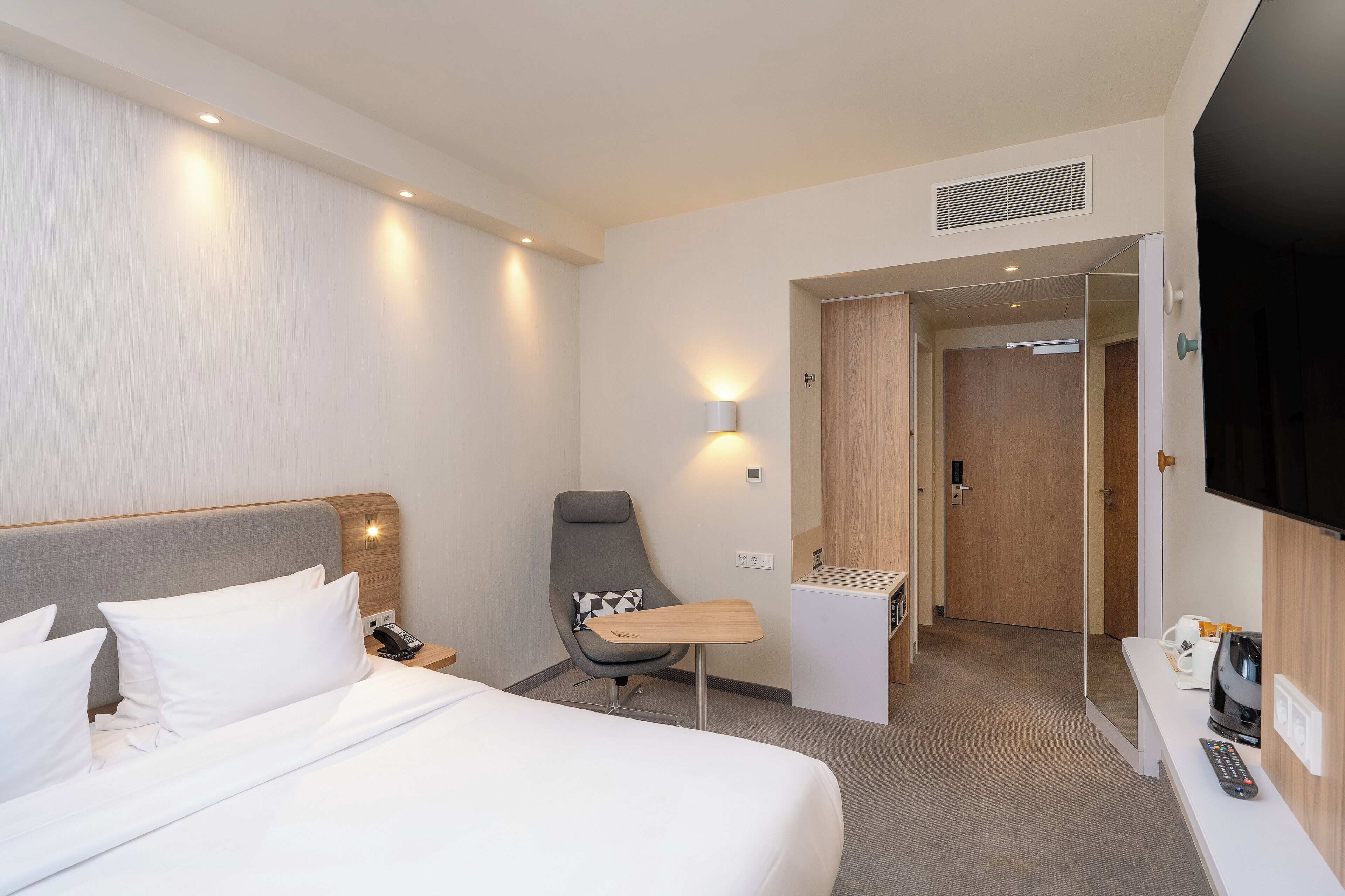 A hotel room with a bed, a desk, a chair, a TV, and a mirror.