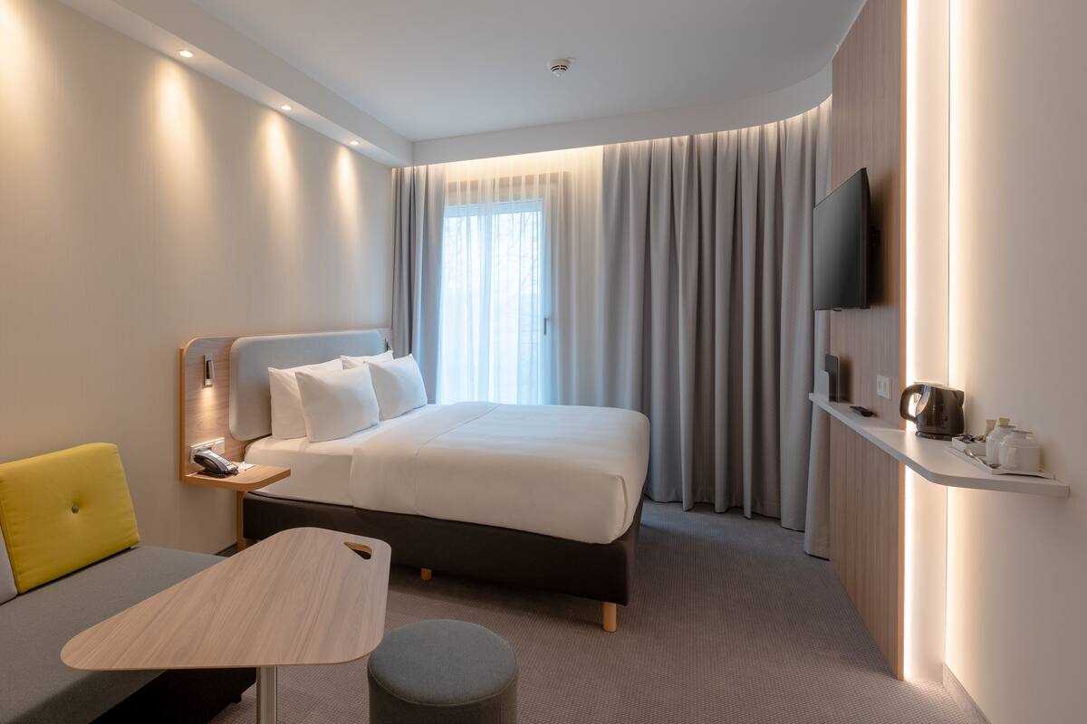 A modern hotel room with a bed, a sofa, a small table, and a TV.