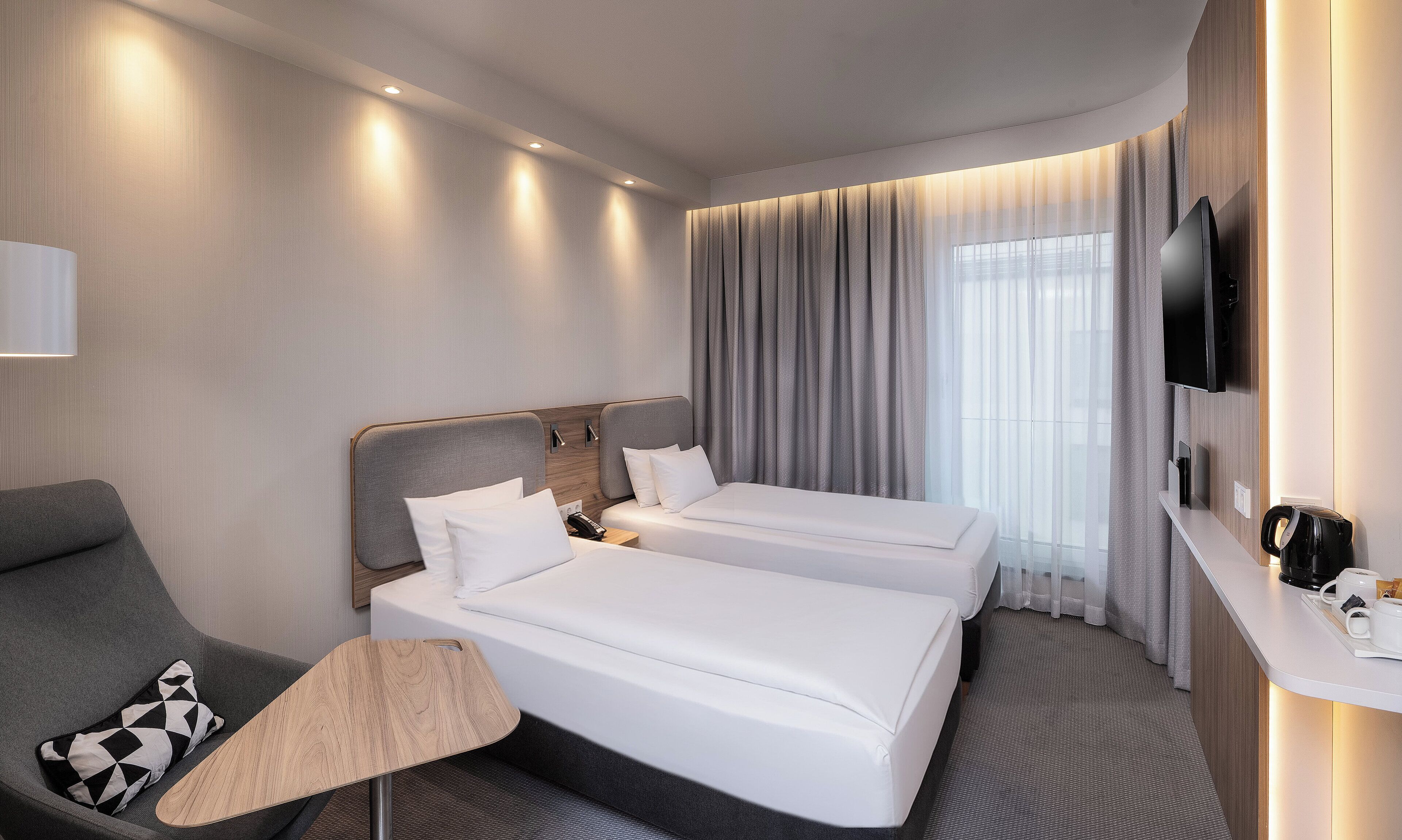 A hotel room with two beds, a TV, a desk with a coffee maker, and a chair.