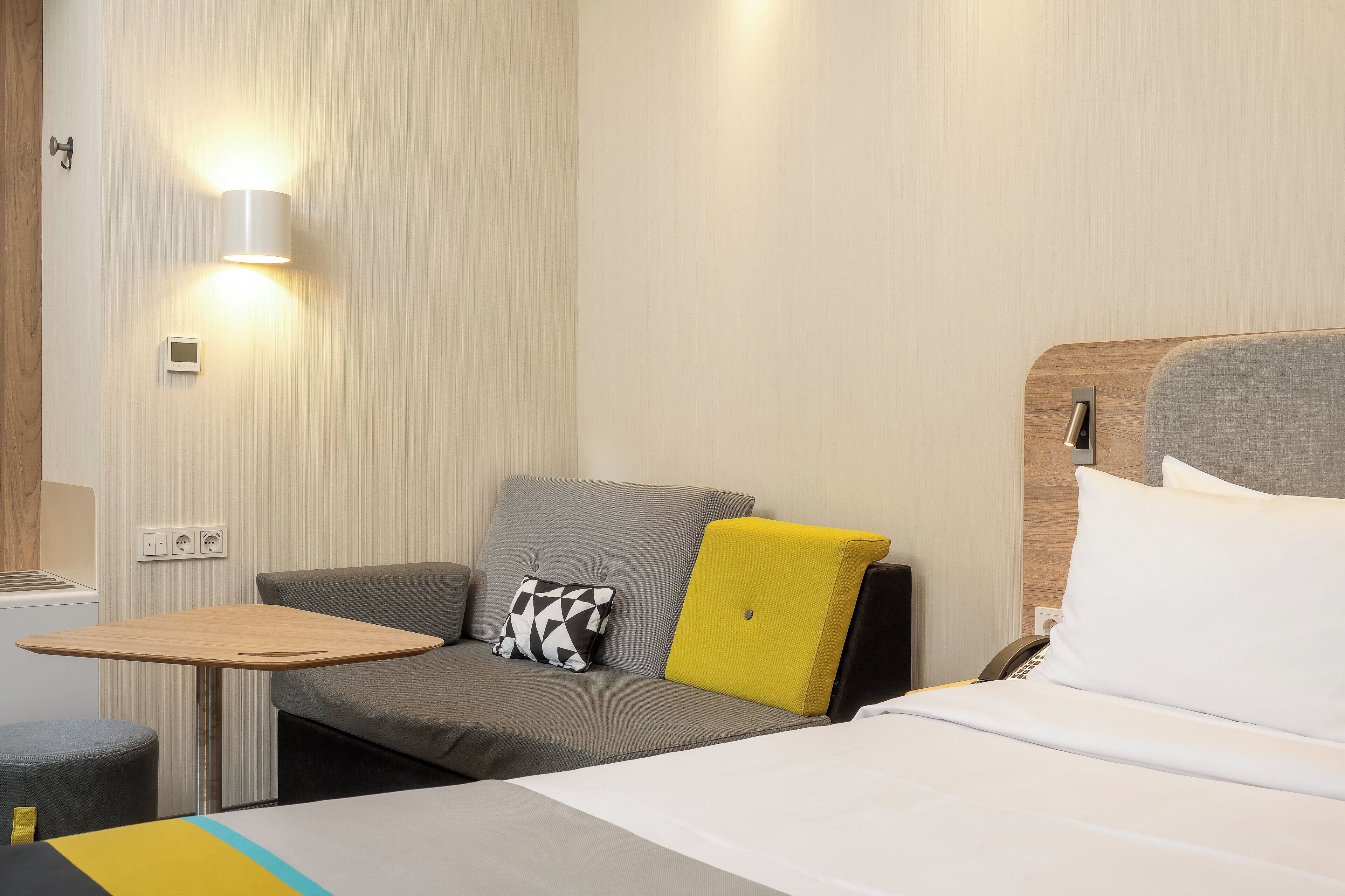 Une chambre d’hôtel moderne équipée d’un lit, d’un canapé, d’une petite table et d’une lampe fixée au mur.