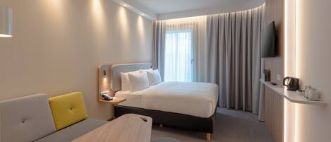 Habitación de hotel moderna con una cama, un sofá, una mesita y un televisor.