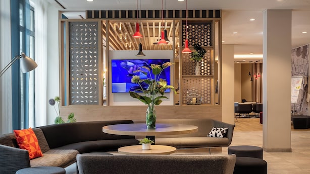 Un hall d’hôtel moderne doté d’un grand téléviseur à écran plat, de sièges confortables et d’une plante décorative placée au centre.