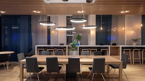 Une salle de conférence moderne, dotée d’une longue table, de nombreuses chaises, de luminaires suspendus et d’une plante en pot.