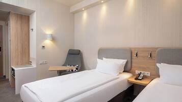 A hotel room with a bed, bedside table, chair, and a small kitchenette.