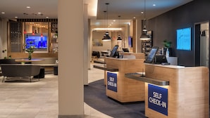 Un hall d’hôtel moderne doté de bornes d’enregistrement automatisées, d’espaces de détente et d’un téléviseur diffusant les actualités.