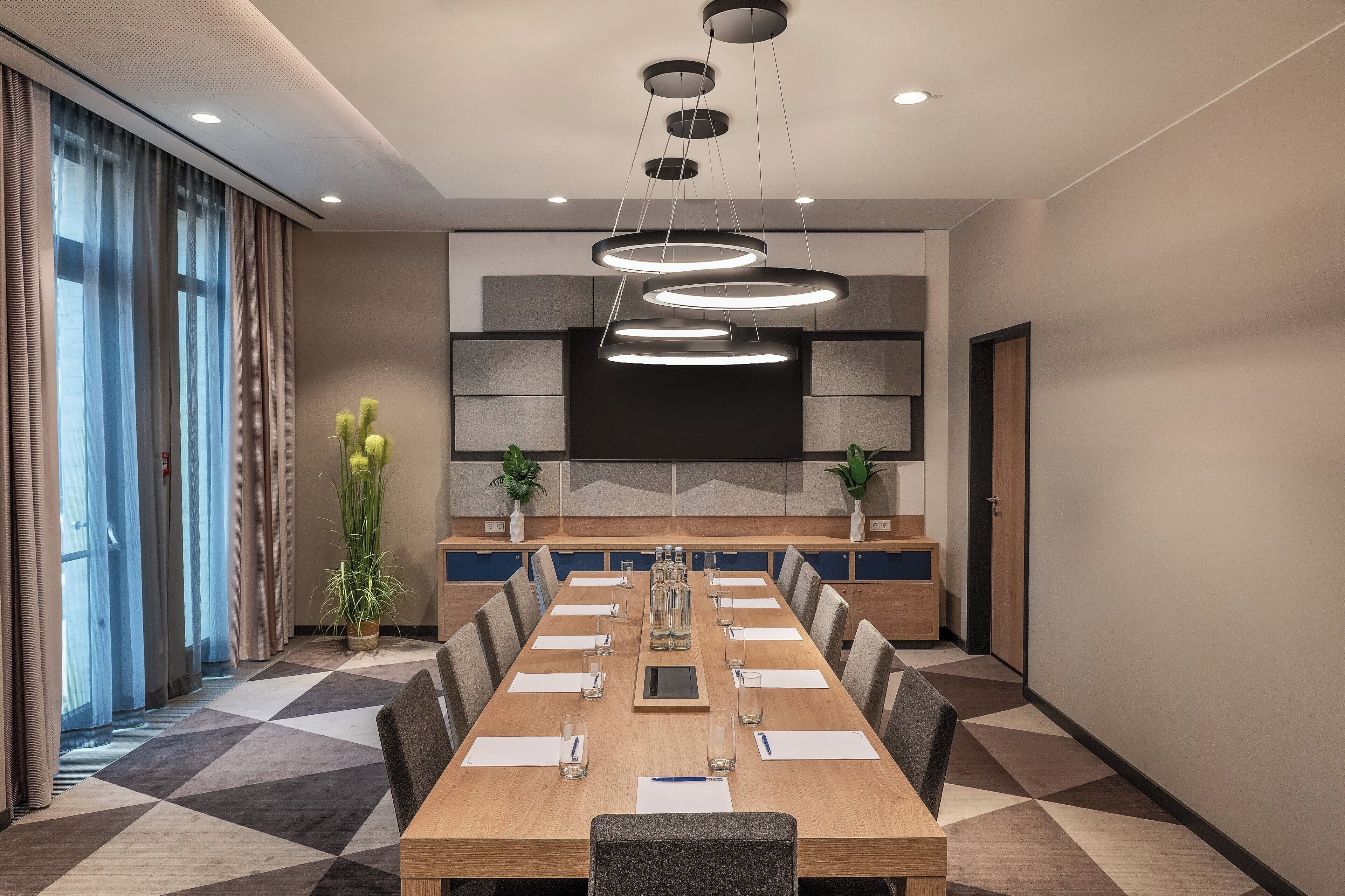 A conference room with a long table, chairs, a large screen, and a plant.