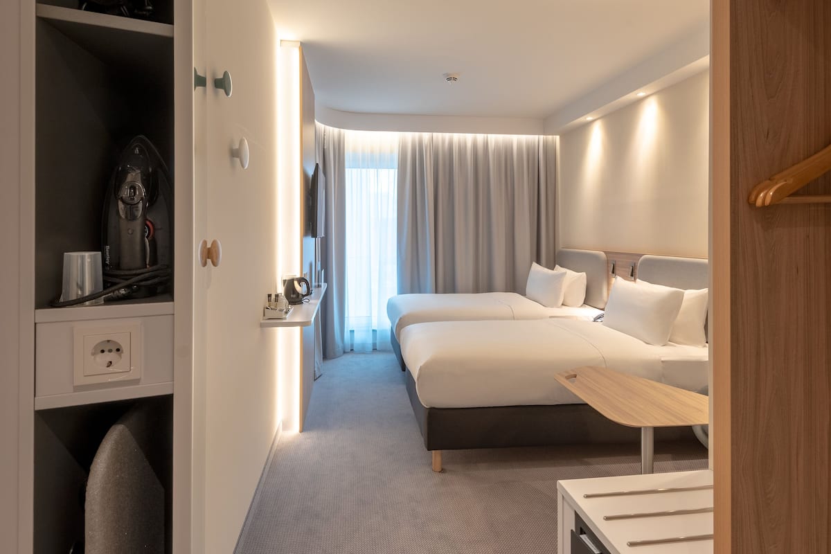 A modern hotel room with a bed, bedside table, and a wardrobe.