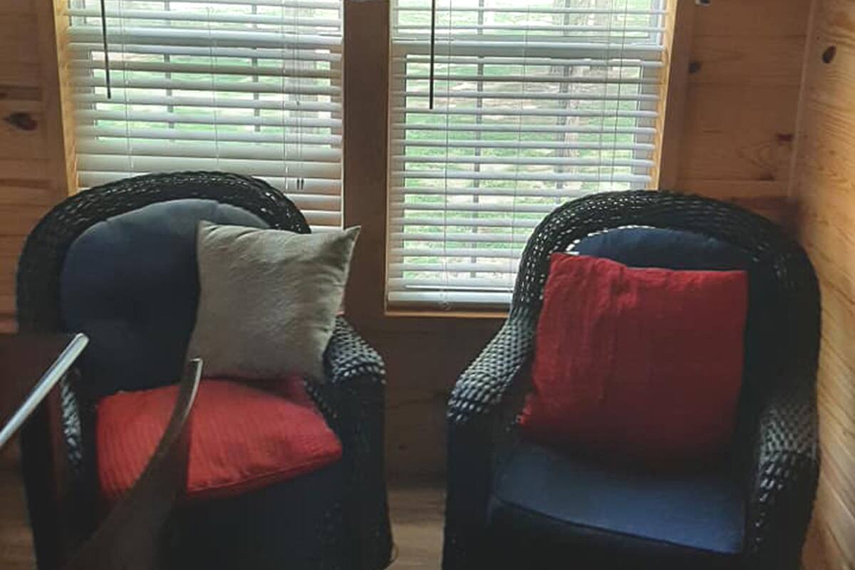 Two wicker chairs with cushions, positioned in front of a window with blinds.