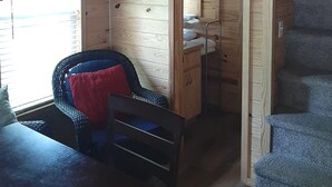 A wooden cabin interior with a bed, a chair with cushions, a small desk, and a ship's wheel decoration. - Birdsong Resort Marina Lakeside RV (Camden)