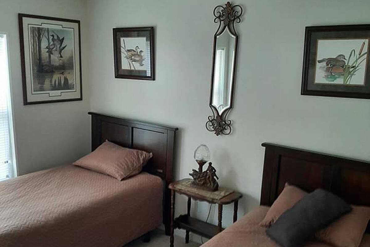 A room with two beds, each with a headboard and a pillow. There is a small table with a decorative item on it, and a mirror on the wall.