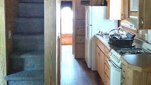 A compact kitchen with a stove, sink, and refrigerator. A wooden staircase leads to an upper level. - Birdsong Resort Marina Lakeside RV (Camden)