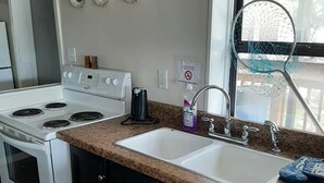 A kitchen with a white stove, a sink, and dark cabinets. - Birdsong Resort Marina Lakeside RV (Camden)