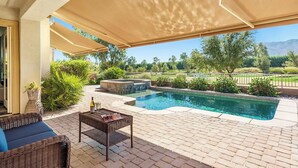 A covered outdoor area with a pool, wicker furniture, and a view of a landscaped garden. - Trilogy  Desert Oasis with Salt Water Pool and Jacuzzi with beautiful Mtn Views (La Quinta)
