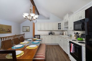 A dining area with a wooden table set for four, white cabinets, a black microwave, and a green kettle.