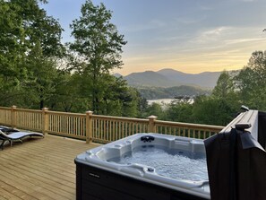 A hot tub on a wooden deck with a view of a lake and mountains.