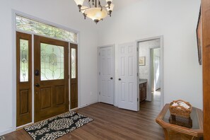 A hallway with wooden flooring, a patterned rug, a wicker basket on a glass table, and white doors with glass panels.
