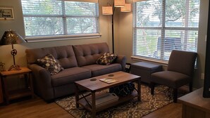 Un salon avec un canapé marron, des coussins à motifs, une table basse en bois, un fauteuil gris, un téléviseur et un tapis à motifs.
