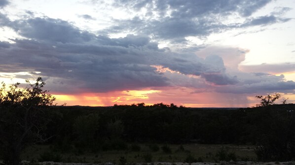 A sunset over a landscape with a cloudy sky and a silhouette of trees in the foreground. - The Cowhouse, a cozy hilltop guesthouse at Barkspin Oaks Ranch. Beautiful views! (Dripping Springs)
