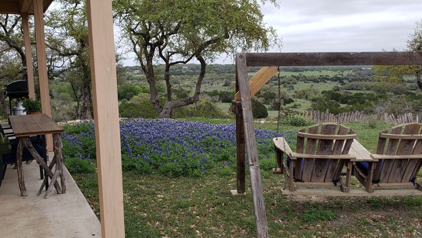 Un espace extérieur aménagé dans un style rustique, avec une table et des chaises en bois, entouré d’un jardin luxuriant et offrant une vue panoramique sur des collines verdoyantes.