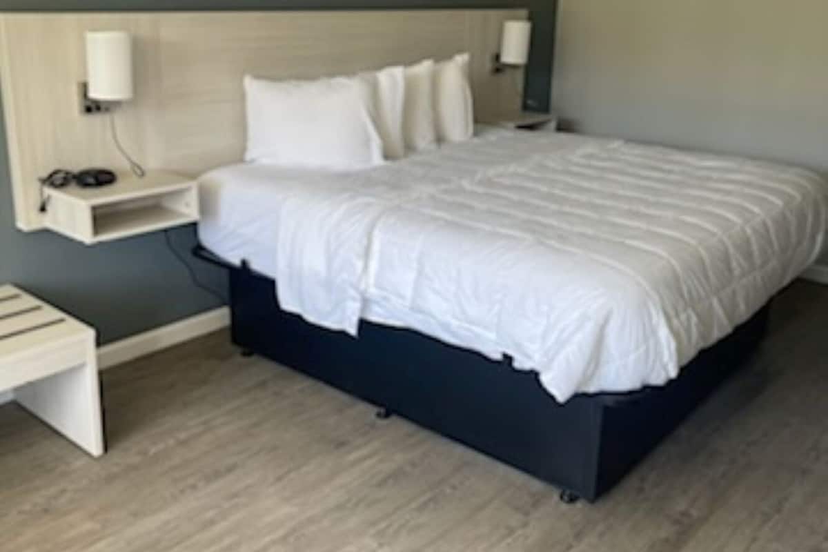 Een keurig opgeruimde hotelkamer met een groot bed, nachtkastjes en een hoofdeinde.